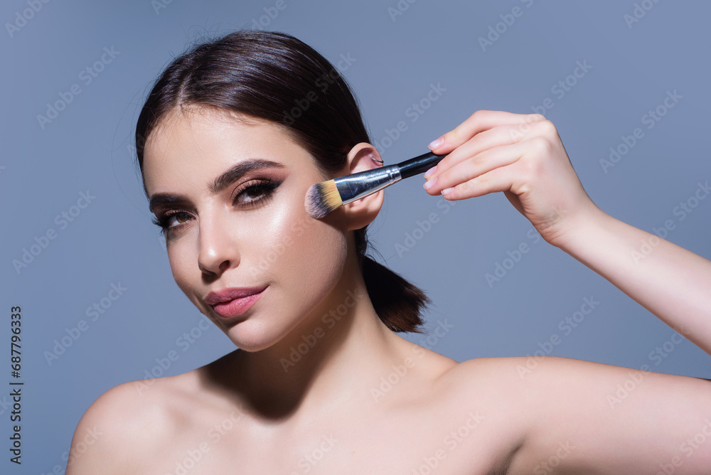 Fototapeta premium Powder brush. Girl hold blusher, apply powder visage with brush, isolated studio background. Young woman powdering cheeks. Makeup brush. Female model gets blush powder with brush.