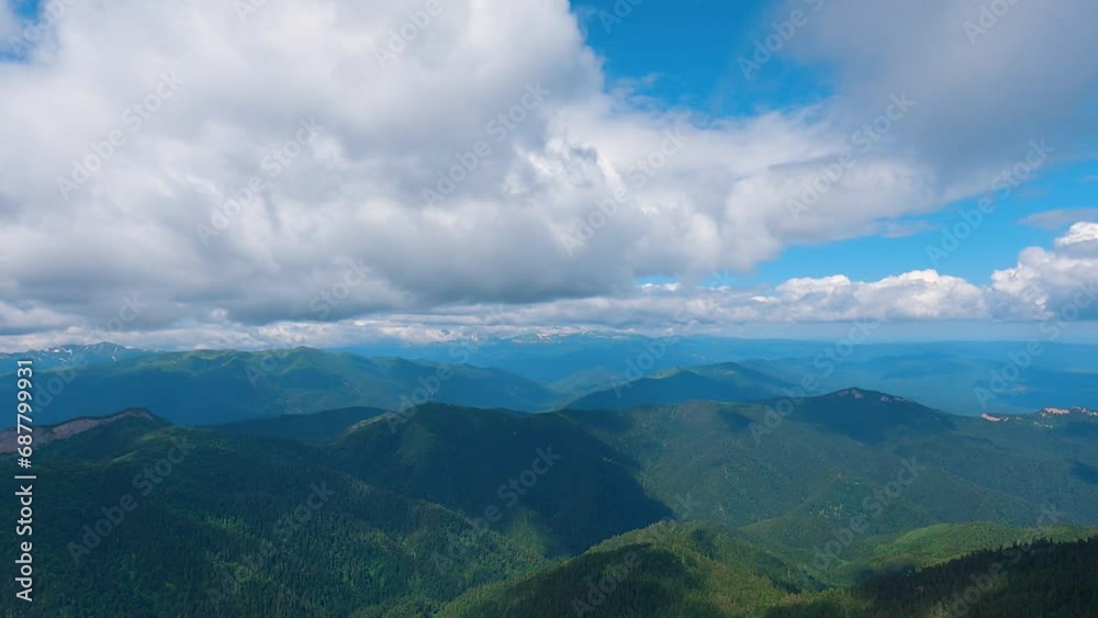 Panoramic view of mountain peaks and cloudy sky. The camera pans from right to left. There are mountains with green trees in the foreground and mountain peaks in the background Panoramic view of mountain peaks and cloudy sky. The camera pans from right to left. There are mountains with green trees in the foreground and mountain peaks in the background