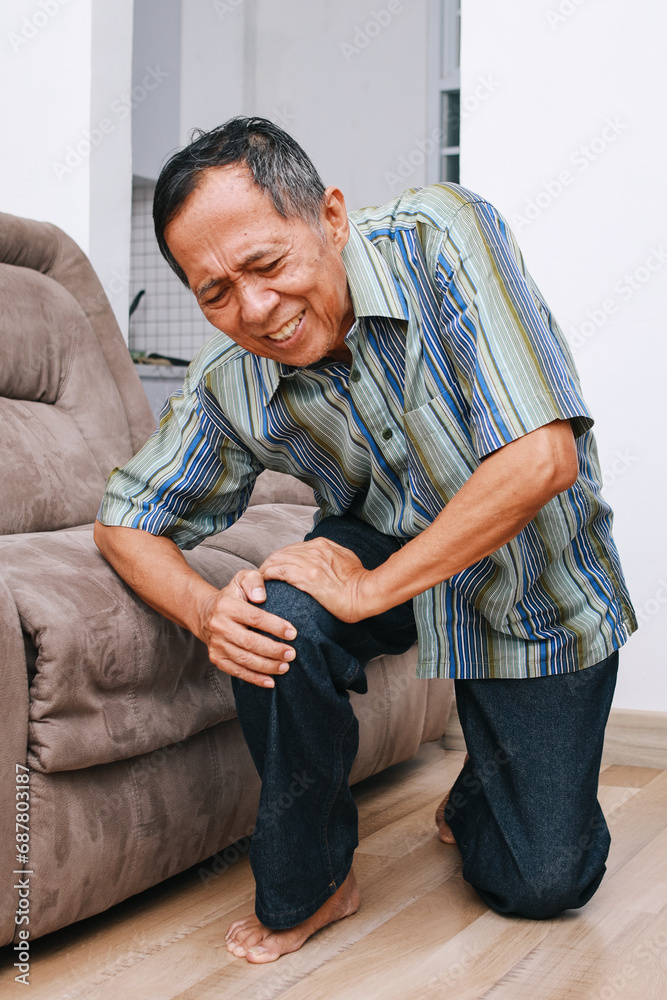 Fototapeta premium Unhappy elderly senior man suffering from knee ache at home