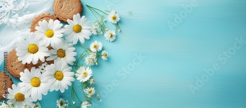 A biscuit with chamomile flowers on parchment in the frame. Turquoise tablecloth with daisies on the table.