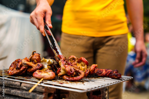 Barbecue with grilled chicken and sausages. People in casual clothes are cooking and holding a glass of beer.