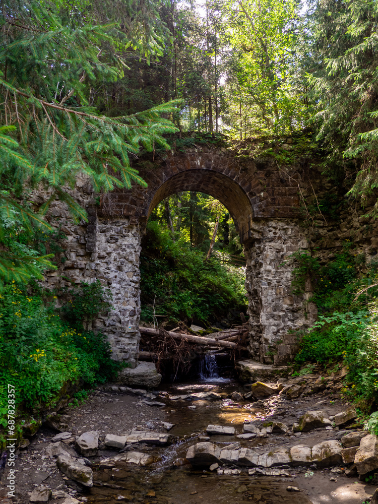 Picturesque ruins of the narrow-gauge viaduct carriage bridge in the village of Vorokhta, Carpathian Mountains, Ukraine. Old stone arched destroyed bridge over small river in a mountain forest.