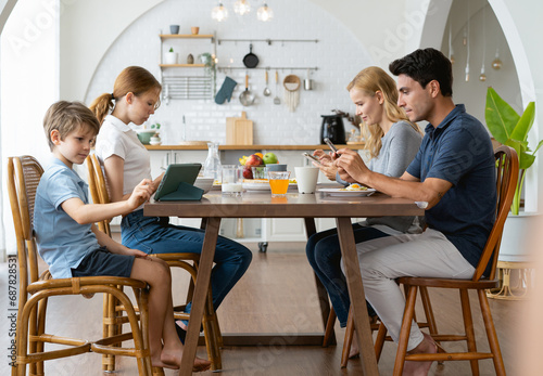 Father and Mother using smartphones and children using digital tablet and mobile phone while having breakfast at table in the morning at home. Family Phubbing And Gadget Addiction Issue