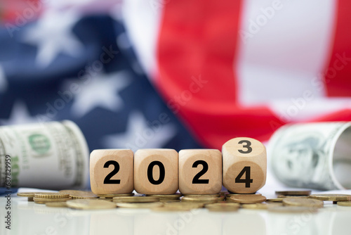 Wooden cubes with text 2024 over the American flag background with coins and banknotes.Starting the new year 2024. United States presidential election 2024.Politics and Voting Conceptual. photo