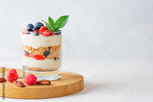 Parfait in a glass with berries, mint, whipped cream and biscuit on a wooden board. Healthy food, vegan, sugar, gluten and lactose free.