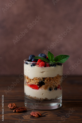 Parfait in a glass with berries, mint, whipped cream, biscuit and pecan on a brown background. Healthy food, vegan, sugar, gluten and lactose free.