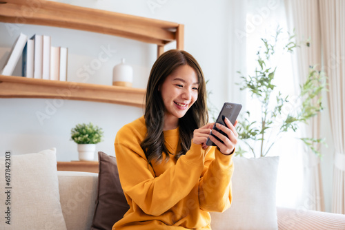 Obraz na plátně Happy young asian woman relax on comfortable couch at home texting messaging on