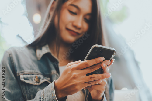 Close-up image of young asian woman sitting at cozy cafe and using modern smartphone device, female hands typing text message via cellphone
