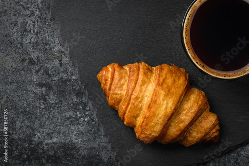 Coffee cup and fresh croissant on black background. Close up view.