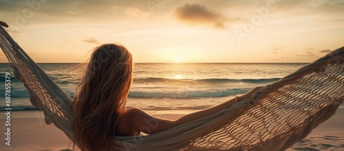 Young woman relaxing in a hammock on a sandy beach enjoying the sunset over the waves of the Indian ocean photo