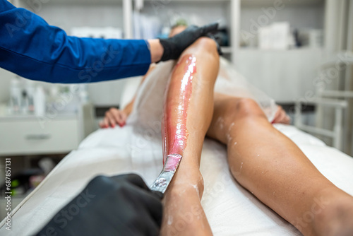 Master of depilation doing applying of sugar paste for the procedure of epilation hair removal on leg photo