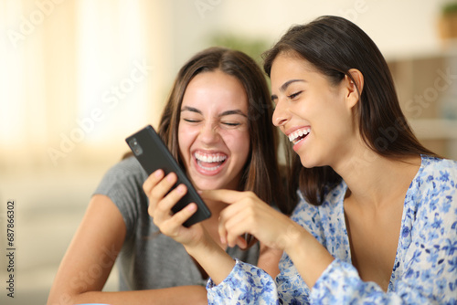 Two joyful roommates laughing watching media on phone