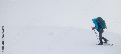 Climber in the mountains. A girl with a backpack and snowshoes walks through the snow.