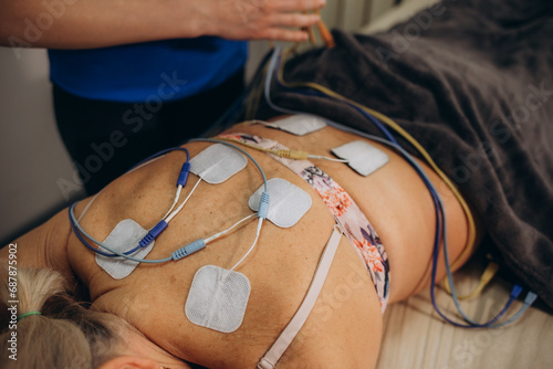 Lower Back Physical Therapy with TENS Electrode Pads, Transcutaneous Electrical Nerve Stimulation. Electrodes onto Patient's Lower Back photo