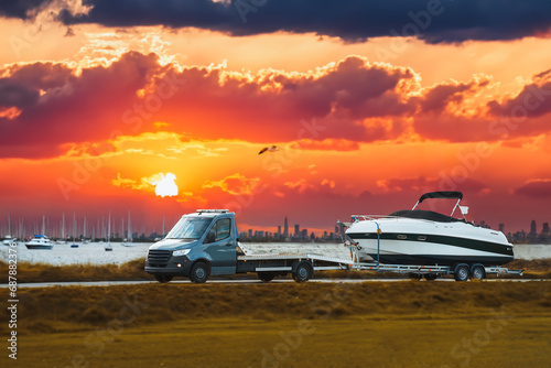 Luxury Boat Journey on the Road. Light-duty truck is hauling a Luxury Motor Boat at Sunset. Close-up of a medium-sized new yacht is being delivered to the customer.