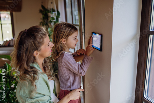 Fotografía Girl helping mother to adjust, lower heating temperature on thermostat