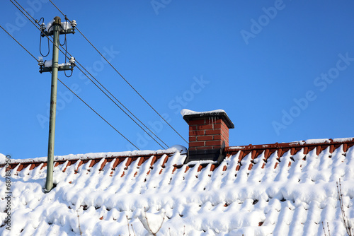 Urban air pollution, Smoke coming out of a brick chimney on a tiled roof with snow on in winter, bright sunshine, blue sky, 