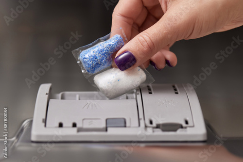 female hand puts dishwasher tablet into automatic dishwasher machine. Close-up