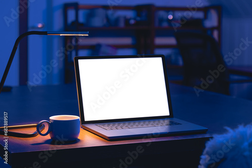 Laptop and cup on a table in a dark room with a blank screen at night.