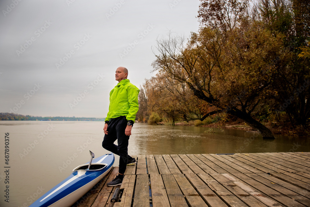 A middle-aged man standing on the jetty and ready to go kayaking on the river