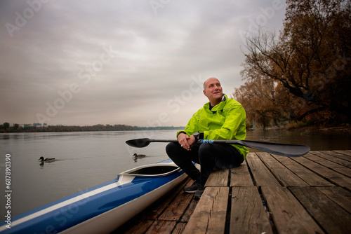 A middle-aged man sitting on the jetty and ready to go kayaking on the river