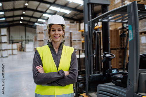 Female warehouse worker standing by forklift. Warehouse manager checking delivery, stock in warehouse, inspecting products for shipment.