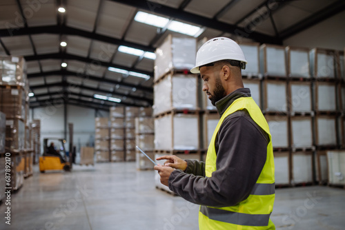 Warehouseman with tablet checking delivery, stock in warehouse. Warehouse manager using warehouse management software, app.