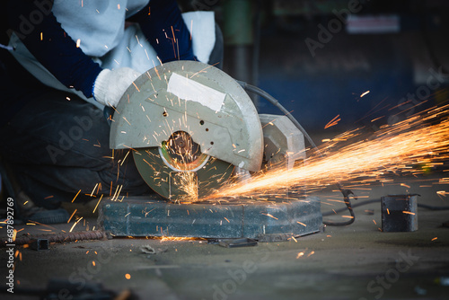 Heavy Industry Engineering Factory Interior with Industrial Worker Using Angle Grinder and Cutting a Metal Tube. Cutting metal and steel with a combination circular saw with a sharp round blade. photo
