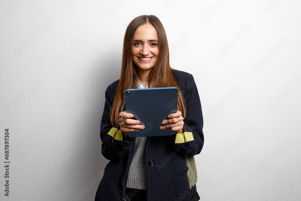 Well-groomed young office woman with brown hair dressed in a striped jacket holds a tablet in her hands Well-groomed young office woman with brown hair dressed in a striped jacket holds a tablet in her hands