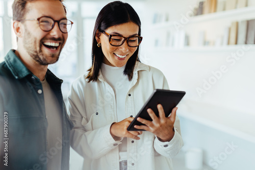 Female designer standing with her colleague and using a tablet