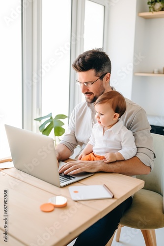 Father working with his baby boy in home office with laptop. Work from home concept 