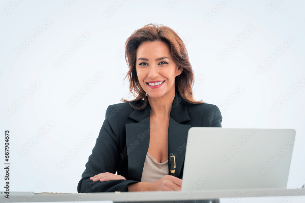 Studio shot of an attractive mid aged businesswoman sitting at desk and using laptop against isolated background Studio shot of an attractive mid aged businesswoman sitting at desk and using laptop against isolated background