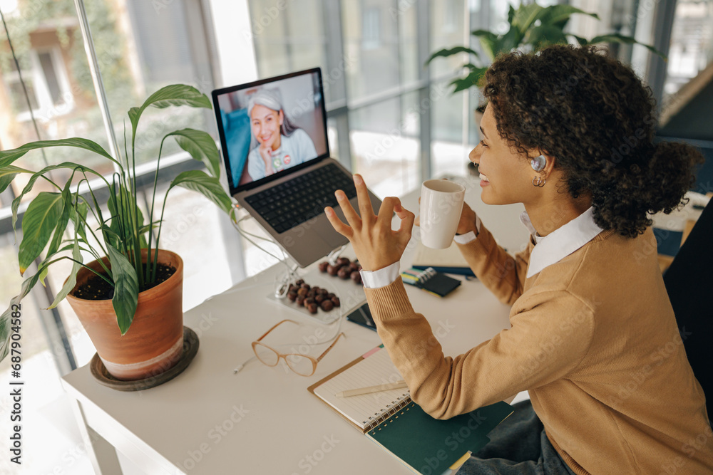 Female freelancer have video conference with client and showing sign Ok sitting in cozy coworking