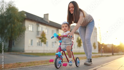 mother teaches daughter to ride. happy family kids dream concept. young mother teaches her daughter small tricycle along the city center road. young mother teaches her little daughter to ride bicycle