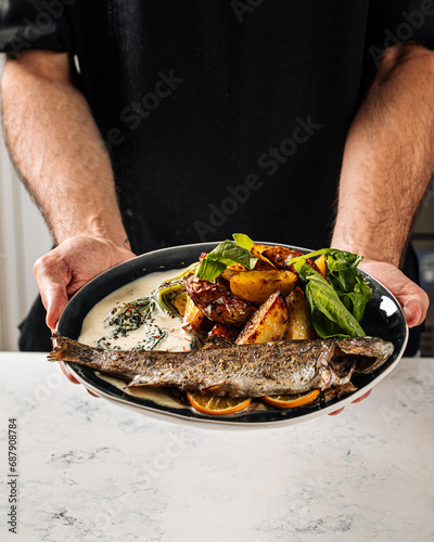 Chef holding cooked grilled fish with potato and sauce