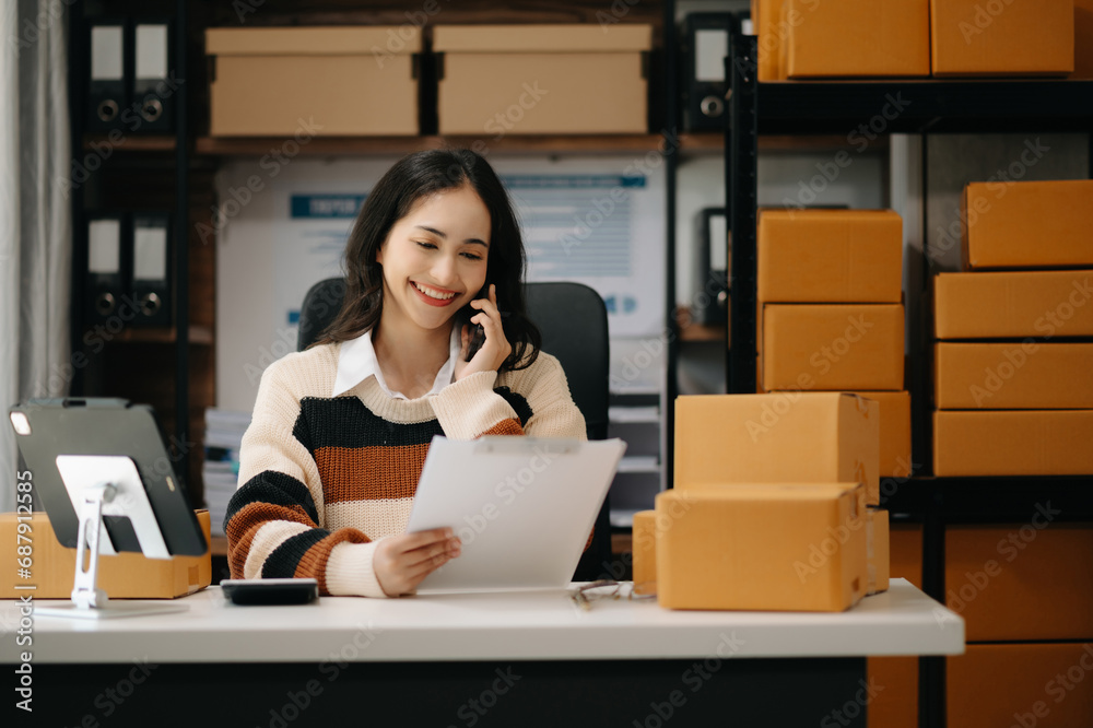 Startup small business SME, Entrepreneur owner woman using smartphone or tablet taking receive and checking online purchase shopping order to preparing pack product box. .. Startup small business SME, Entrepreneur owner woman using smartphone or tablet taking receive and checking online purchase shopping order to preparing pack product box. ..