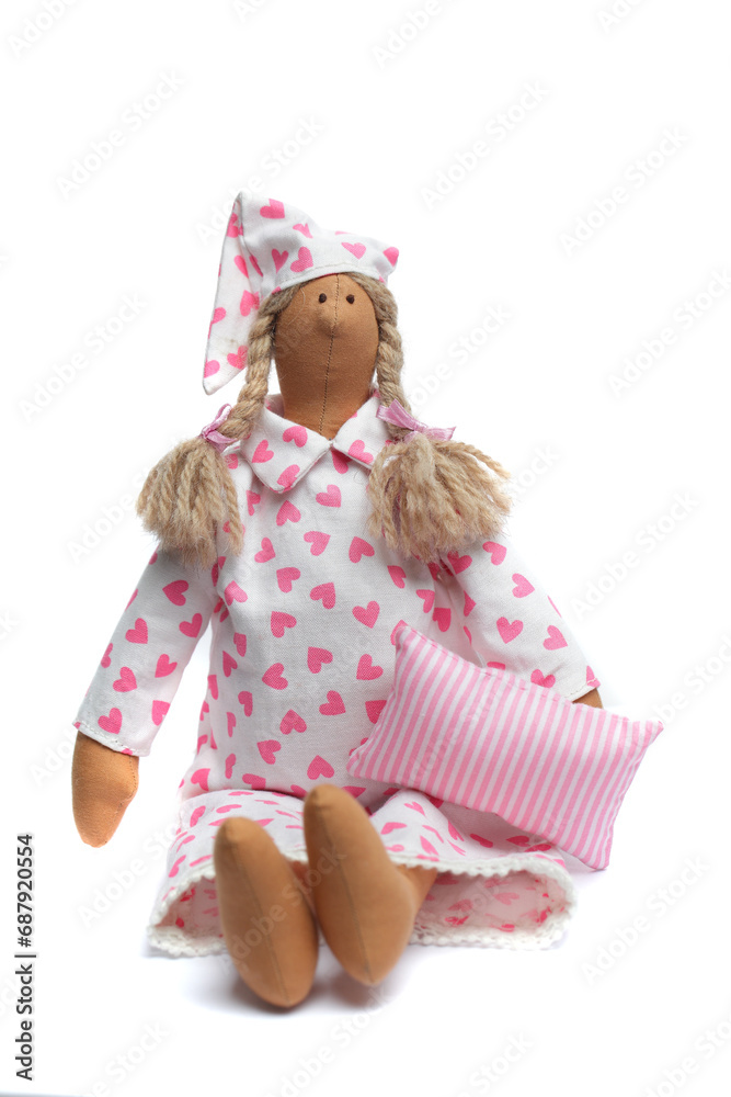 Funny handmade doll in pajamas dress holding pillow on white. Toy maded pink color natural cotton linen material Funny handmade doll in pajamas dress holding pillow on white. Toy maded pink color natural cotton linen material