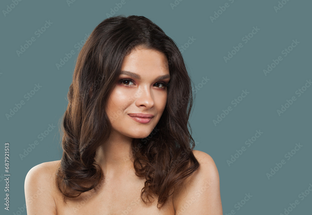 Naklejka premium Cheerful young model woman with wavy dark brown hairstyle and fresh clean shiny skin on blue studio background, fashion portrait. Skin care, hair care and cosmetology concept