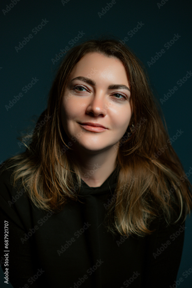 Classic dark studio portrait of a young brown-haired woman in black clothes sitting on a chair. Classic dark studio portrait of a young brown-haired woman in black clothes sitting on a chair.