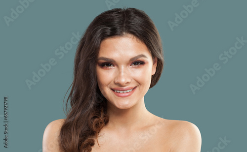 Happy young model woman with wavy dark brown hairstyle and fresh clean shiny skin on blue studio background, fashion portrait. Skin care, hair care and cosmetology concept