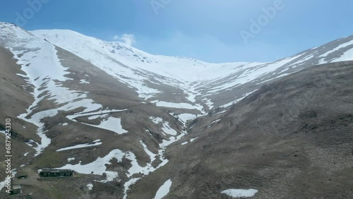 Aerial view of high mountains covered with snow with thawing on a sunny day against a blue sky. Deserted gray mountains in winter without grass with snowy peaks. Drone footage. Direct flight. Armenia