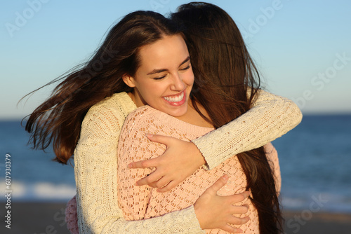 Two happy friends hugging at sunset on the beach photo