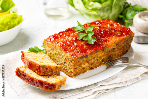 Meatloaf or terrine with chicken and turkey meat, carrot, leek and green peas, glazed with ketchup. Baked minced chicken meat. White table surface.