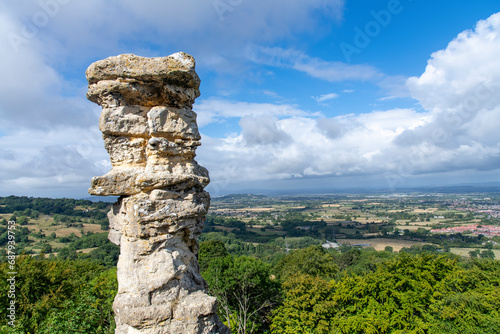 Close up view of limestone rock formation Devil’s Chimney against backdrop of panoramic view from Leckhampton Hill, Cheltenham, UK along the public footpath Cotswold Way overlooking the Cotswolds photo