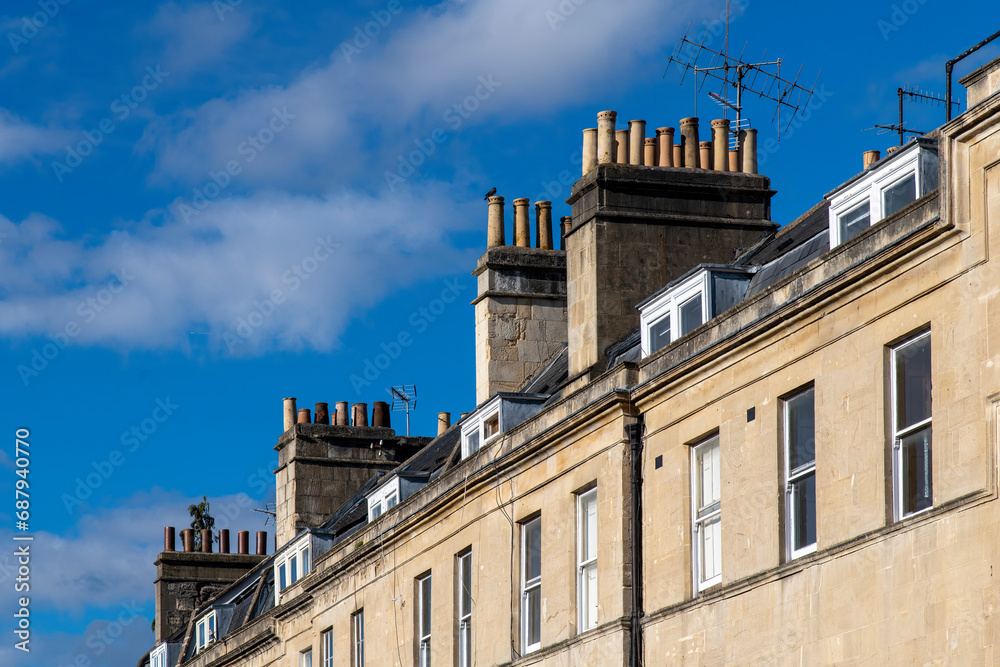 Low angle view of characteristic roofs and chimneys of Georgian townhouses in Bath, Sommerset, UK against a white clouded blue sky