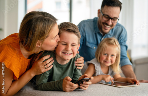 Happy young family having fun time at home. Parents with children using digital device.