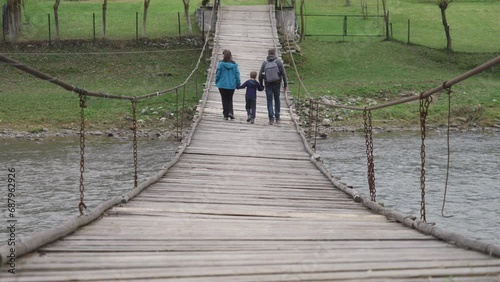 Parents with child hiking on suspended rope bridge in the wild nature