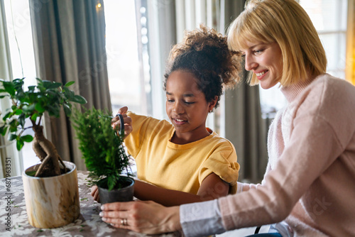 Happy caucasian mother and her adopted african american daughter taking care of plants indoors. photo