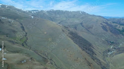 Aerial view of high mountains covered with snow with thawing on a sunny day against a blue sky. Deserted gray mountains in winter without grass with snowy peaks. Drone footage. Movement in an arc