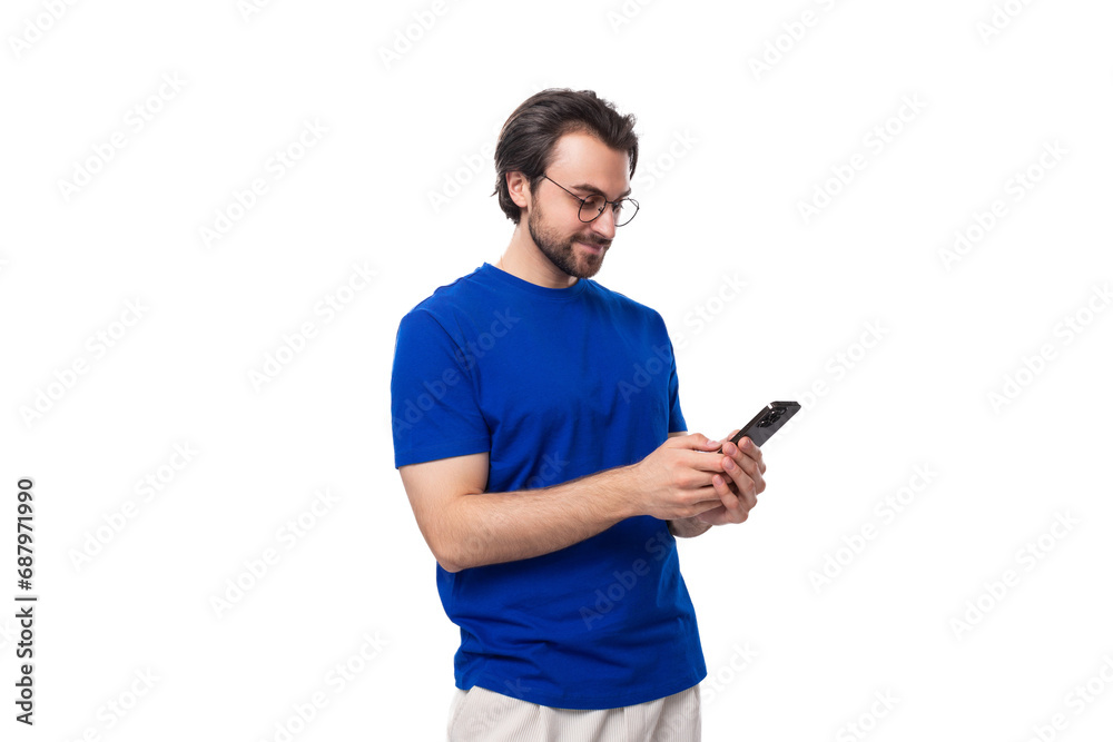 portrait of a young caucasian brunette man with a stylish hairstyle and beard in a blue t-shirt holding a phone in his hands portrait of a young caucasian brunette man with a stylish hairstyle and beard in a blue t-shirt holding a phone in his hands